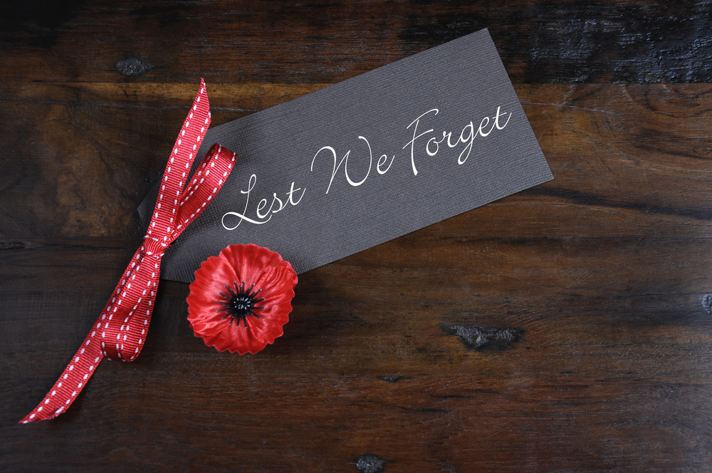 Lest We Forget, Red Flanders Poppy Lapel Pin Badge for November 11, Remembrance Day appeal, on dark recycled wood background.