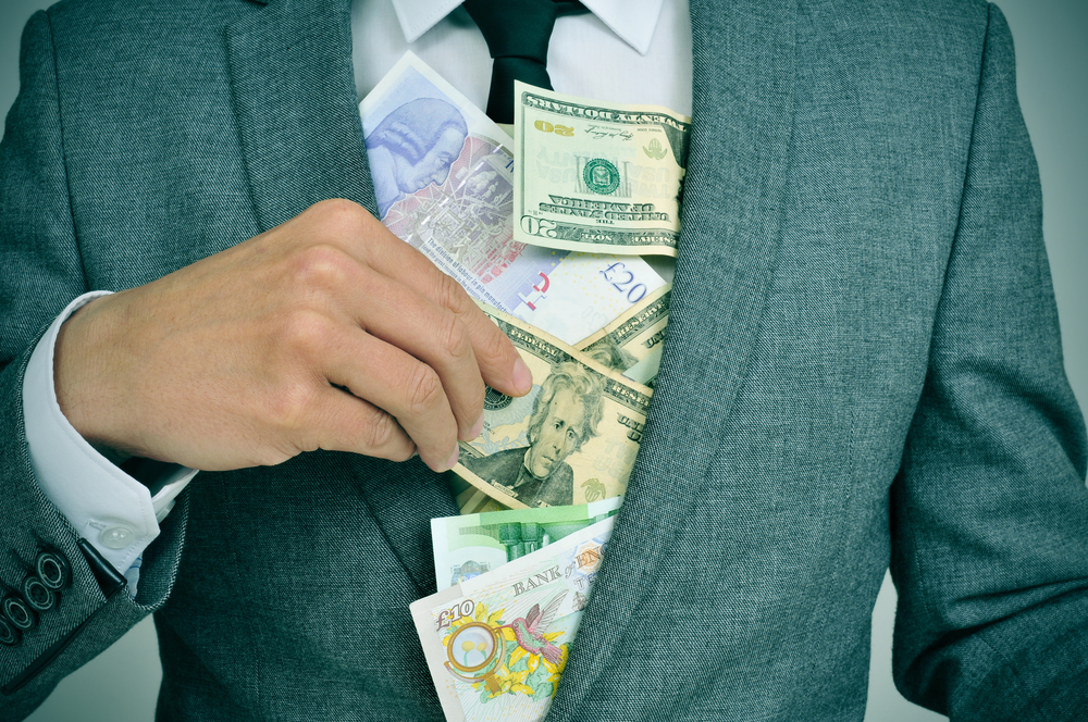 man in suit putting euro, dollar and pound bills in his jacket, depicting concepts such as greediness, corruption or misappropriation