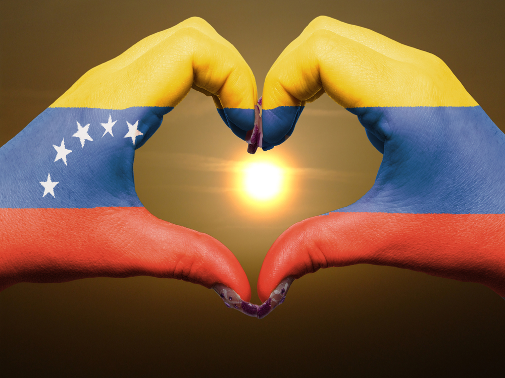 Tourist gesture made by venezuela flag colored hands showing symbol of heart and love during sunrise
